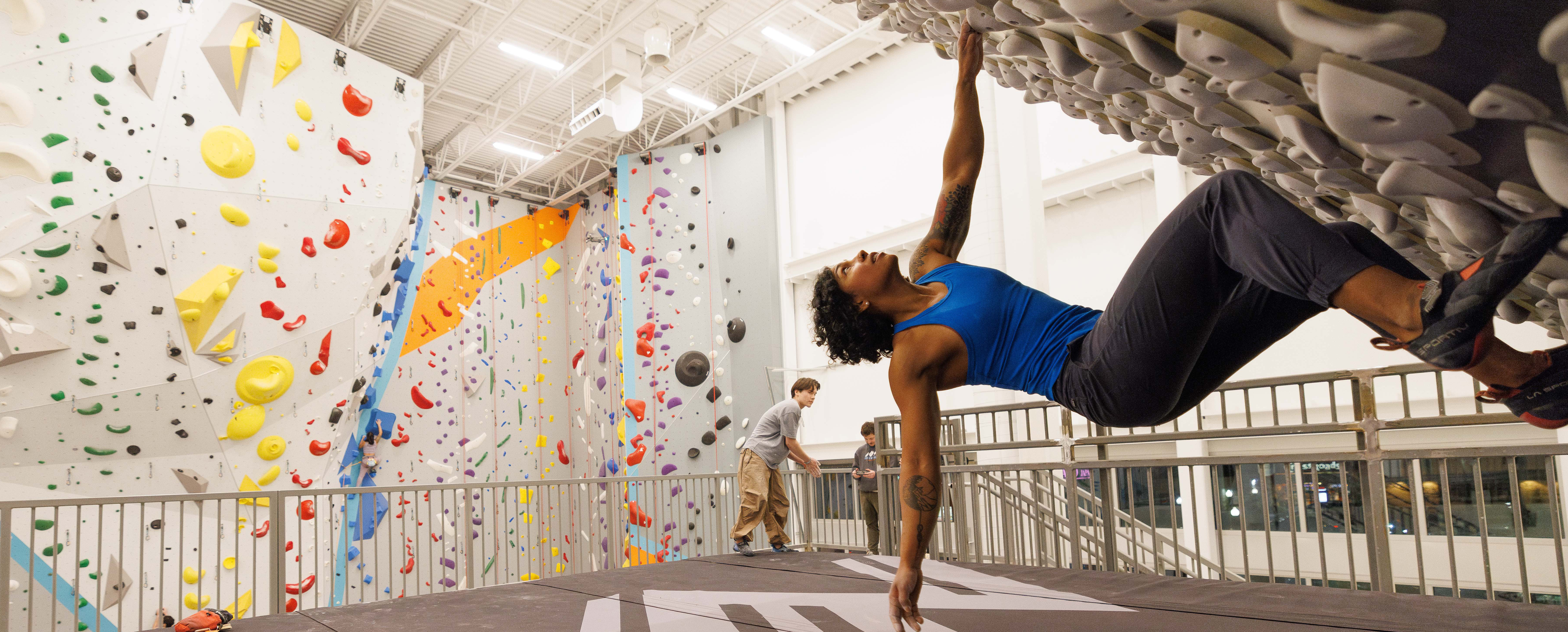 woman climbing kilter board with climbing walls in background